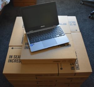 Pile of Chromebook in boxes with one open on the top. 