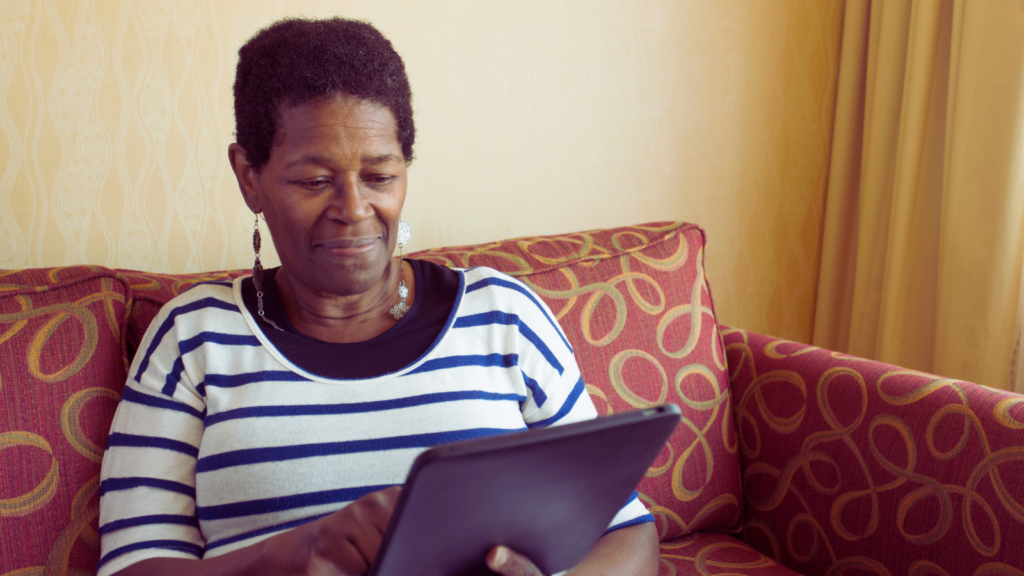 A woman is sat on her sofa looking an her iPad,