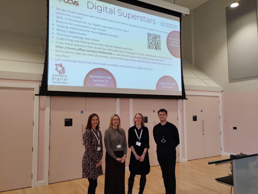 Karen, Jo, Sally and Will standing in front of a big screen that has a Powerpoint projected onto it. The Powerpoint text reads: Digital Superstars