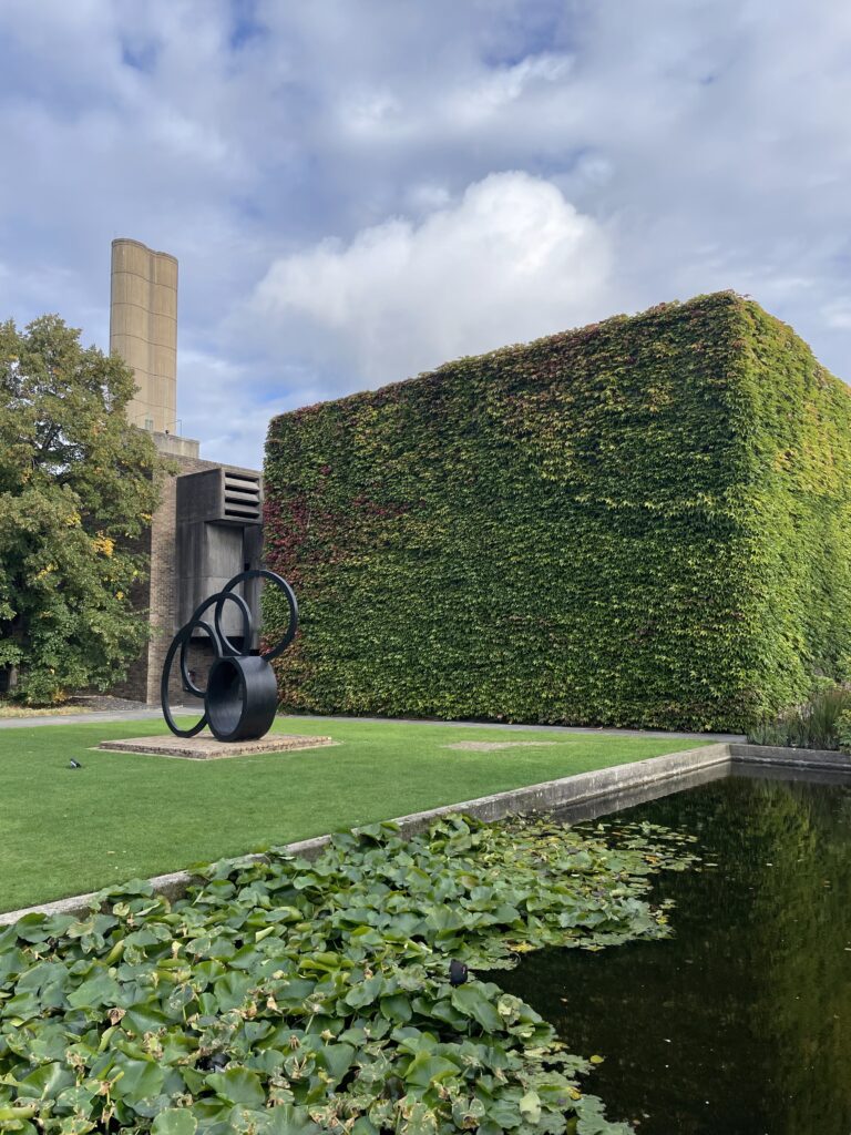 Churchill Colle grounds. Garden and pond with lily pads, we also see a sculpture.