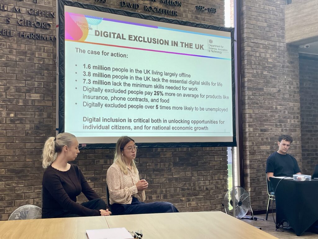 Two people sat in front of a big screen showing a Powerpoint presentation.