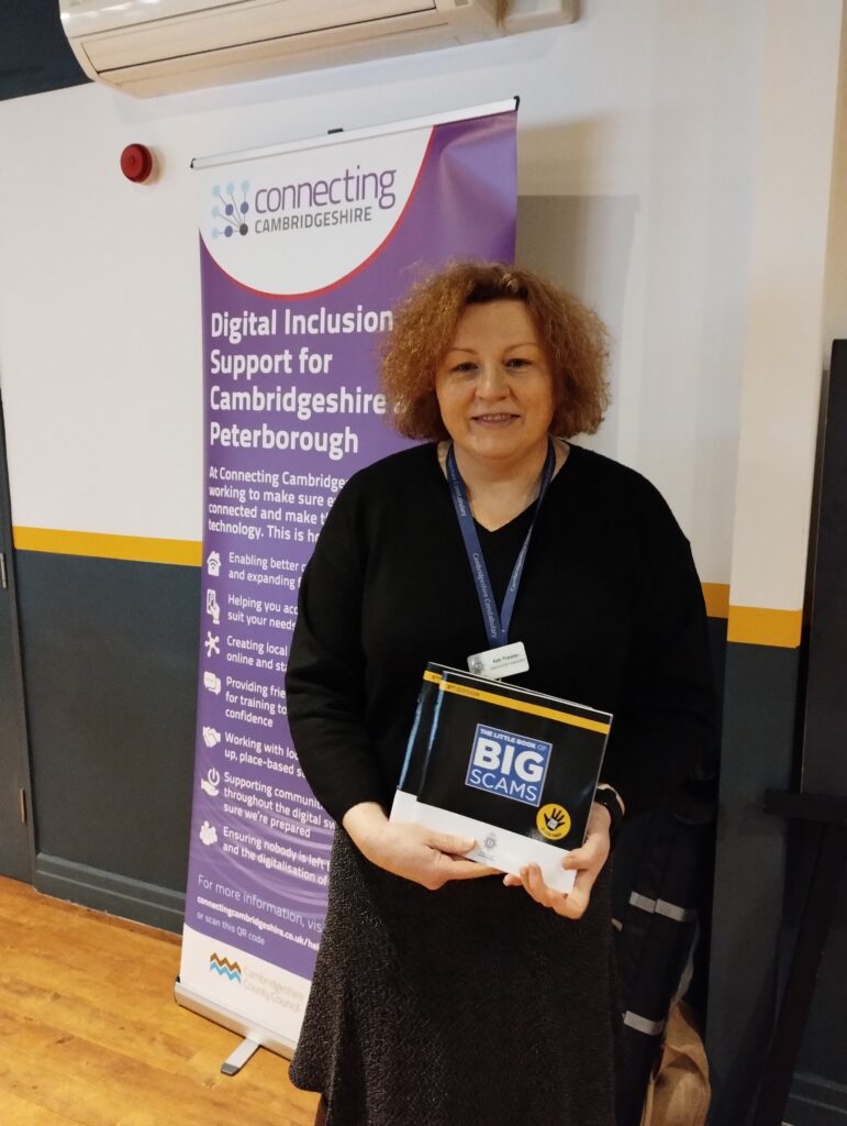 A woman holds a SCAM booklet in front of a Connecting Cambridgeshire roller banner.